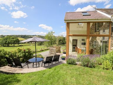 A garden patio with chairs a table and umbrella next to a glass wall room at Llety'r Wennol Ffarmers near Lampeter