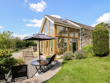 Stone house with large windows and outdoor seating with umbrella in garden at Llety'r Wennol Ffarmers near Lampeter