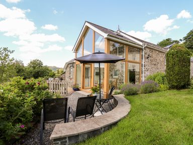 An outdoor patio with chairs a table and umbrellas next to a stone house with large windows at Llety'r Wennol Ffarmers near Lampeter