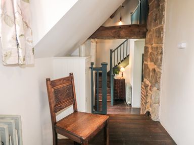 A wooden chair next to a white cabinet under a sloped ceiling near stairs with a wooden beam and stone wall at Porters Lodge in Polesworth