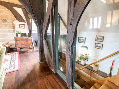 A hallway with wooden beams and flooring next to a staircase with framed pictures and a lamp at Porter's Lodge in Polesworth