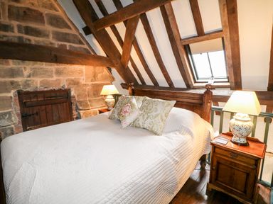 A bedroom with a bed with pillows between two bedside tables with lamps and exposed wooden beams at Porters Lodge in Polesworth