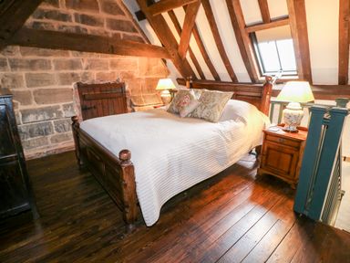 A bedroom with wooden bed frame and white bedding under a sloped ceiling with exposed wooden beams at Porters Lodge in Polesworth