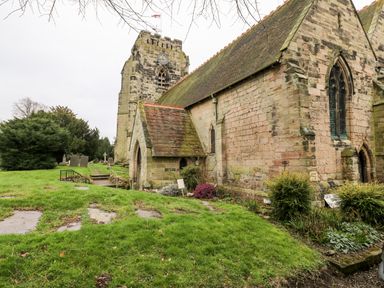 A stone church building with a clock tower and gravestones on grassy grounds at Porter's Lodge in Polesworth