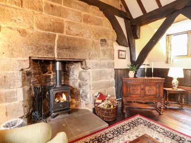 A room with a stone fireplace and wood stove next to a basket of firewood and wooden furniture at Porter's Lodge in Polesworth
