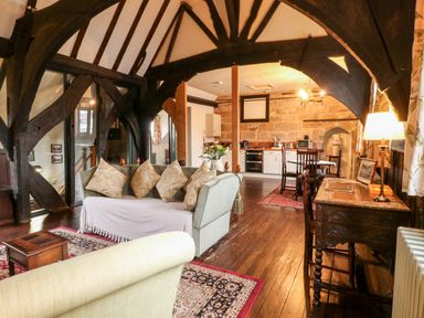 A living area with sofas and cushions a wooden desk with a lamp and chair a dining table with chairs and a kitchen with appliances at Porters Lodge in Polesworth