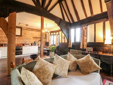 An open living room and kitchen with wooden beams and a sofa with cushions at Porters Lodge in Polesworth