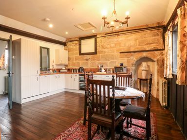 A kitchen with white cabinets wooden dining table and chairs on a red rug and stone walls at Porters Lodge in Polesworth