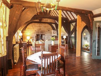 A living room with wooden beams a dining table with chairs and a stone fireplace at Porter's Lodge in Polesworth