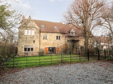 A stone house with a pitched roof and multiple windows behind a black metal fence and a gravel area at Gatehouse Croft in Polesworth