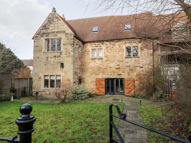 A stone house with wooden shutters on the windows and a tiled roof with a garden and a paved path at Gatehouse Croft in Polesworth