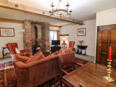 A living room with a wood burning stove a sofa armchairs and a wooden dining table with a red candle at Gatehouse Croft Polesworth