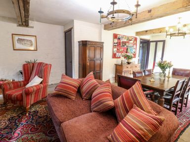 A living room and dining area with wooden table chairs sofa armchair and cushions at Gatehouse Croft in Polesworth