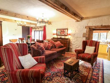 A living room with striped armchairs a sofa with cushions a wooden coffee table and a dining table with chairs at Gatehouse Croft in Polesworth