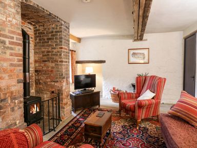 A living room with a brick fireplace a television on a wooden stand upholstered armchairs and a patterned rug at Gatehouse Croft in Polesworth