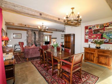 A dining room with wooden table and chairs and a living area with sofas and a brick fireplace at Gatehouse Croft in Polesworth