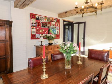 A dining room with a wooden table red candles a flower vase wooden cabinet and a wall hanging at Gatehouse Croft in Polesworth
