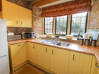 A kitchen with yellow cabinets a stainless steel sink a microwave a bread box and a window with floral blinds at Gatehouse Croft in Polesworth