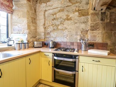 A kitchen with yellow cabinets a double oven a gas stove and stone walls at Gatehouse Croft in Polesworth