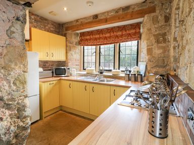 A kitchen with yellow cabinets a microwave stainless steel utensils and a window with red curtains at Gatehouse Croft in Polesworth