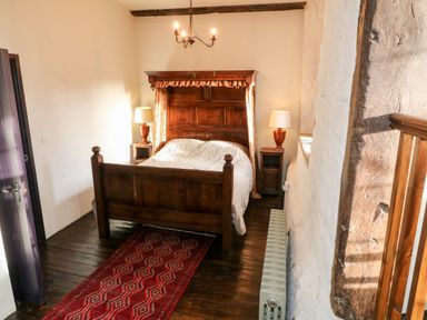 A bedroom with a wooden four poster bed two bedside tables with lamps a red rug and a radiator at Gatehouse Croft in Polesworth