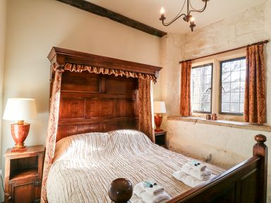 A bedroom with a wooden four-poster bed two bedside tables with lamps and a window with curtains at Gatehouse Croft in Polesworth