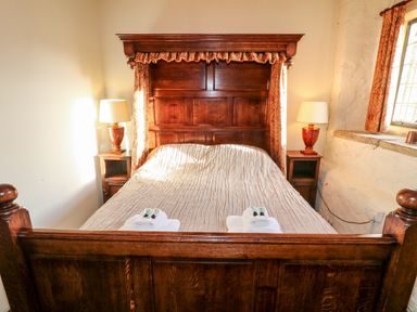 A bedroom with a wooden bed frame two bedside tables with lamps and towels on the bed at Gatehouse Croft in Polesworth