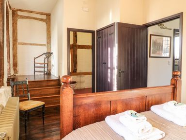 A bedroom with wooden bed and folded towels and chairs near stairs at Gatehouse Croft in Polesworth
