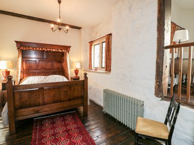 A bedroom with a wooden bed frame two lamps on bedside tables a red patterned rug a black chair and a window at Gatehouse Croft in Polesworth