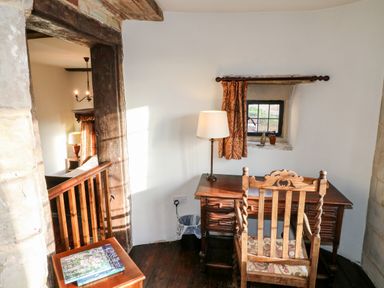 A small room with a wooden desk and chair a table lamp a small window with a curtain and a side table with books at Gatehouse Croft in Polesworth