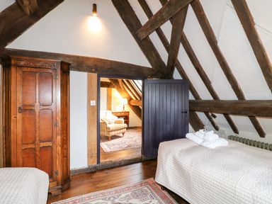 A bedroom with exposed wooden beams a wooden wardrobe and a door leading to a sitting area with an armchair at Gatehouse Croft in Polesworth