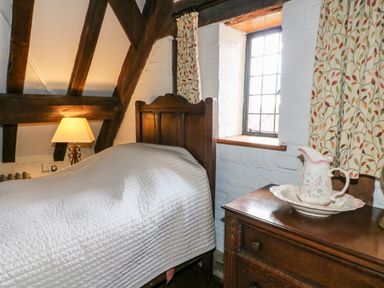 A bedroom with a wooden single bed beside a window and a wooden dresser with a ceramic jug and basin at Gatehouse Croft in Polesworth