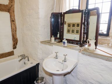 A bathroom with a white sink and a bathtub with wooden paneling at Gatehouse Croft in Polesworth