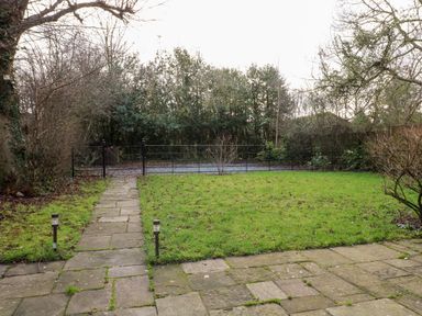 A garden with a stone pathway leading to a black metal gate and grassy area at Gatehouse Croft in Polesworth