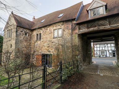 An old stone building with a gated courtyard and an archway leading to a street with a timber framed building at Gatehouse Croft in Polesworth