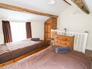 A bedroom with two single beds brown bedding and rolled towels a wooden dresser a chair and a small wardrobe at Penlon in Capel Bangor near Aberystwyth