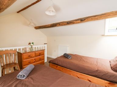 A bedroom with two single beds wooden chest of drawers a wooden chair and exposed ceiling beams at Penlon Capel Bangor near Aberystwyth