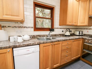 A kitchen with wooden cabinets countertop sink dishwasher kettle toaster and a window at Penlon in Capel Bangor near Aberystwyth