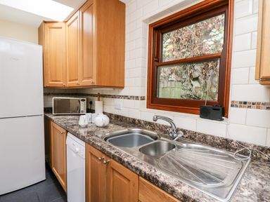 A kitchen with wooden cabinets a double sink a microwave and a refrigerator at Penlon in Capel Bangor near Aberystwyth