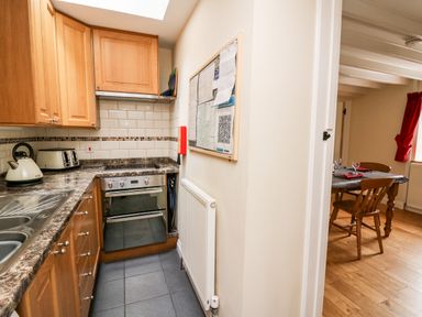 A kitchen with wooden cabinets, a marble countertop, a kettle, a toaster, an oven, and a sink next to a dining area with a wooden table and chairs at Penlon in Capel Bangor near Aberystwyth