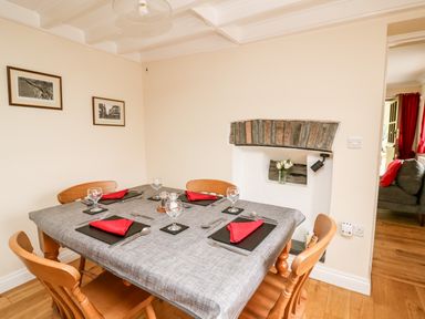 A dining room with a table set for four with red napkins and wooden chairs at Penlon in Capel Bangor near Aberystwyth