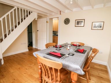 A dining room with a table set for four under stairs and wall clock at Penlon in Capel Bangor near Aberystwyth