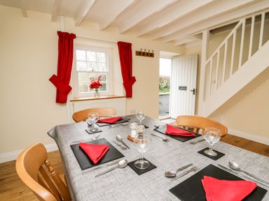 A dining area with a table set with glasses and red napkins near a window with red curtains at Penlon in Capel Bangor near Aberystwyth