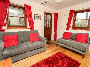 A sitting room with two grey sofas with red cushions and red curtains at Penlon in Capel Bangor near Aberystwyth