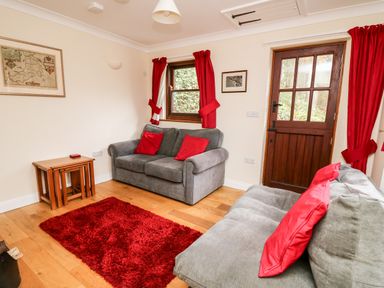 A living room with two gray sofas with red cushions a red rug wooden tables red curtains and a wooden door at Penlon in Capel Bangor near Aberystwyth