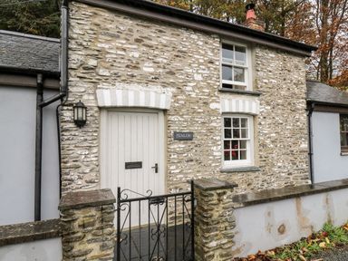 An exterior view of a stone cottage with a white door two windows and a black metal gate at Penlon in Capel Bangor near Aberystwyth