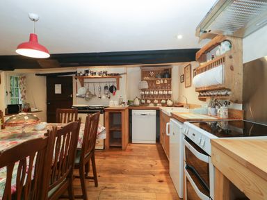 A kitchen with wooden floors cabinets and dining table with chairs at Church Farmhouse in Winsham