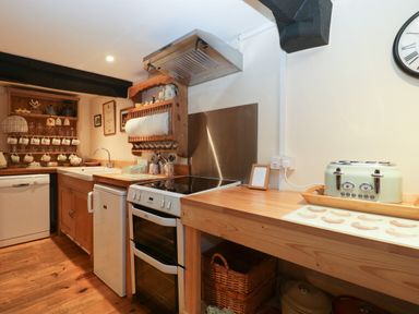 A kitchen with a stove dishwasher toaster wooden countertops and shelves at Church Farmhouse Winsham