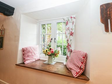 A window seat with red and white checked cushions and a vase of flowers on the wooden sill at Church Farmhouse in Winsham