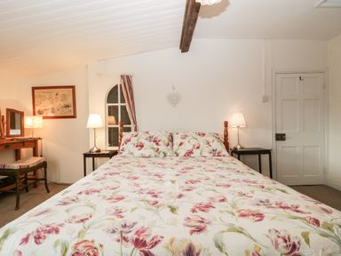 A bedroom with a floral bedspread on the bed two bedside tables with lamps a wooden dressing table with a chair and a door at Church Farmhouse in Winsham